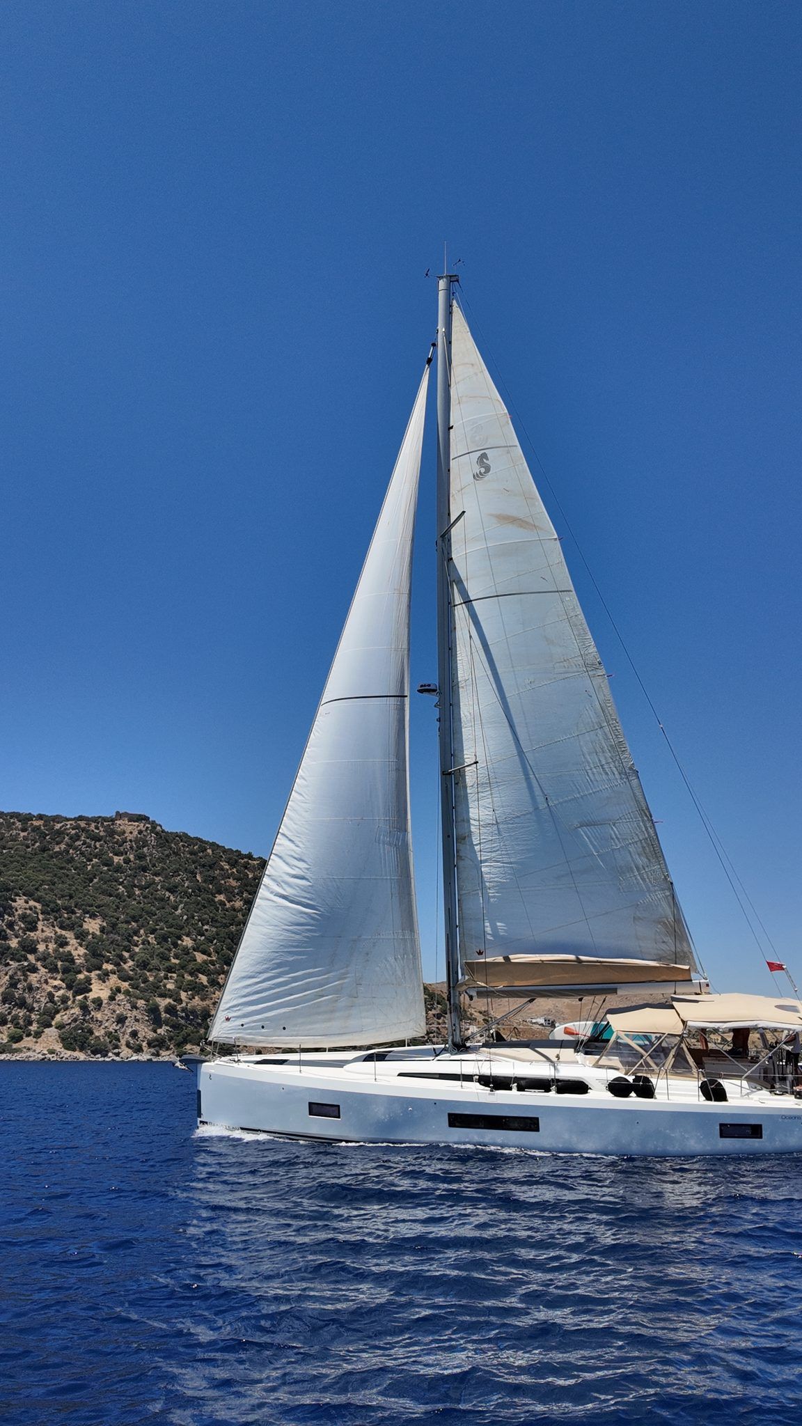 Under full sail, hillside behind
